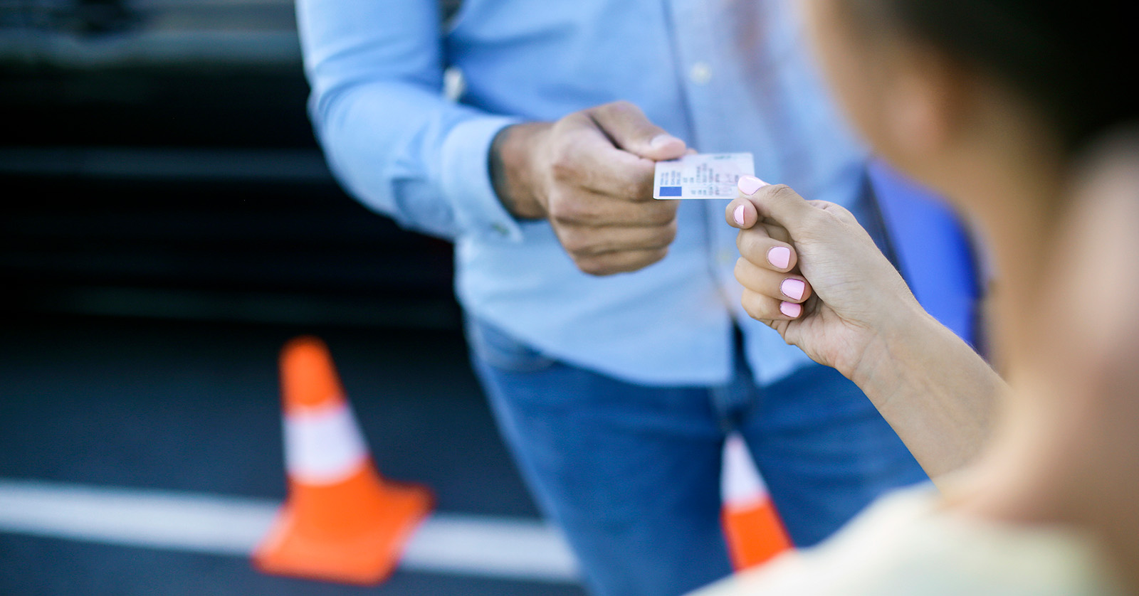 Primer plano de un hombre mayor entregándole una licencia de conducir a una mujer más joven.