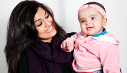 Una mamá sonrie con una bebé en sus brazos.